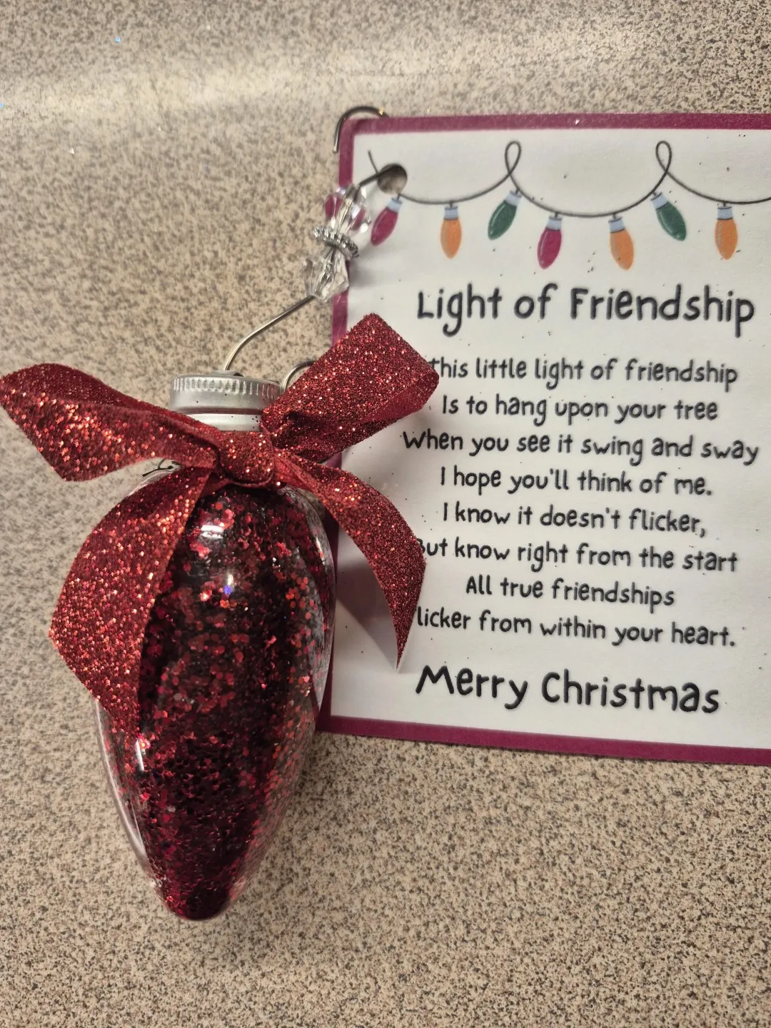 A red ornament shaped like a large christmas light. A message is attached to it with a poem about friendship.