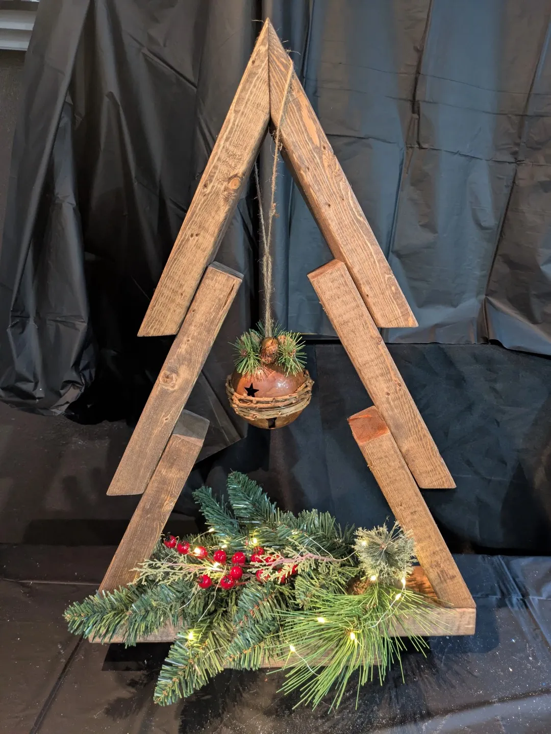 A flat wooden structure in the shape of a christmas tree. It has an ornament hanging from the top, and a wreath at the bottom.
