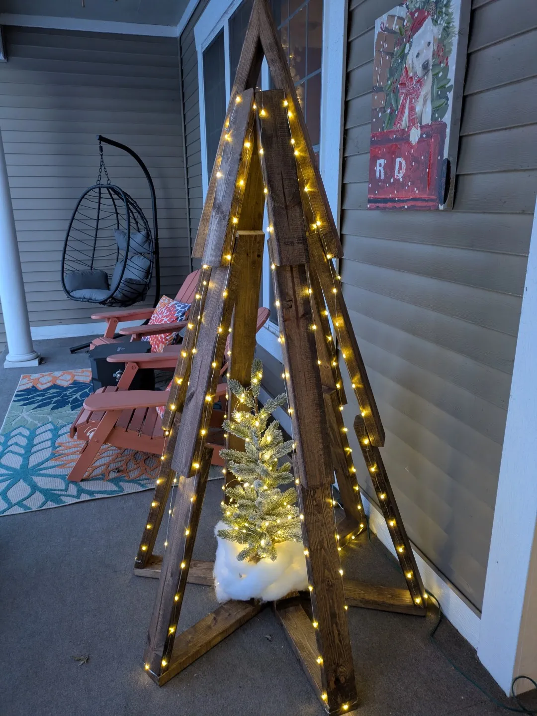 A tall christmas tree structure made out of wood. It has LED lights on it, and a small winter-themed tree at its base.
